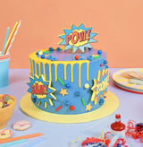 Comic Book Superhero Cake with blue frosting, yellow drip, and comic-style POW!, BAM!, and ZOOM! decorations by Crumbs & Doilies